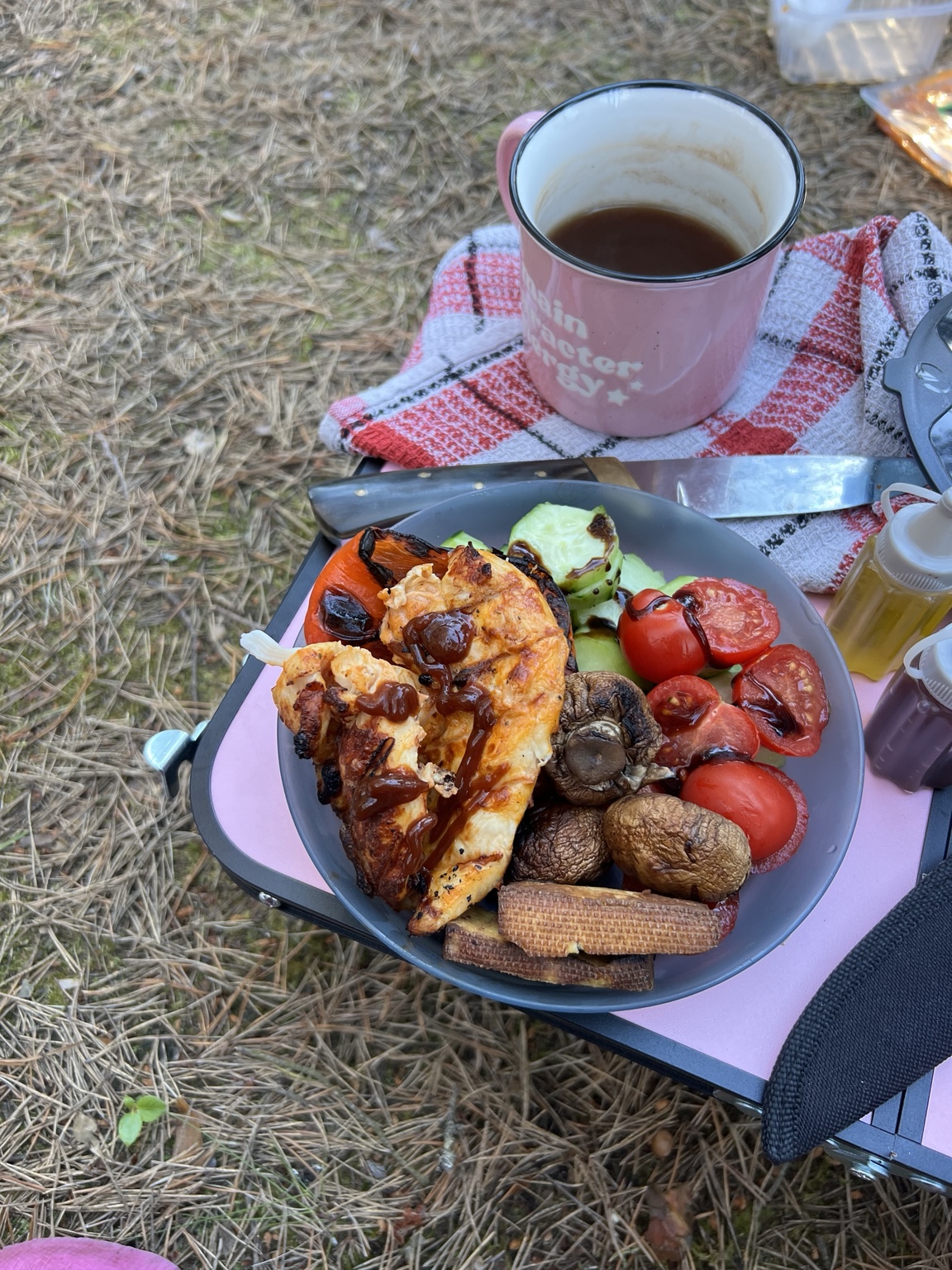 A plate of grilled chicken, vegetables, mushrooms and tofu beside a camping mug