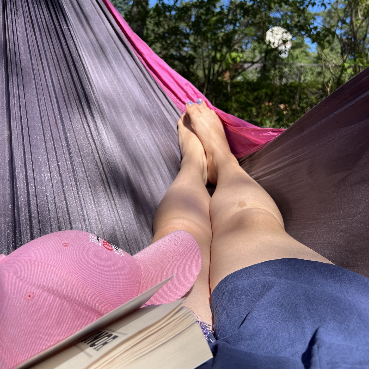 Reading a book in a pink hammock beneath the trees